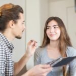 A makeup artist applies eyeshadow to a smiling woman during a vlog recording.